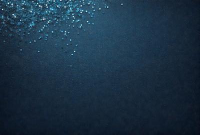 The primary subject of the image is a blue background with a scattering of glittering blue and white beads. The setting is a dark blue background, which contrasts with the bright blue beads. The visual style is a close-up of the beads on the blue background, creating a visually appealing and artistic composition. The colors and mood of the image are predominantly blue, with the glittering beads adding a touch of brightness and sparkle to the overall atmosphere.