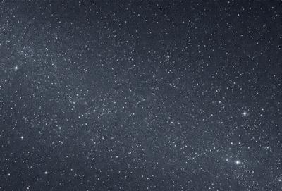 The primary subject of the image is the night sky, which is filled with stars. The setting is a dark, star-filled sky, and the visual style is a photo of the night sky. The colors and mood of the image are predominantly dark and serene, with the stars providing a sense of depth and beauty.