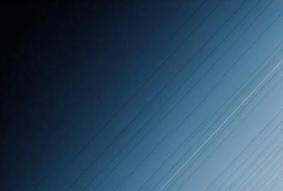 The primary subject of the image is a series of power lines against a blue sky. The setting is a clear day with no clouds, providing a bright and sunny atmosphere. The visual style is a photo, capturing the power lines and sky in a realistic manner. The colors and mood are predominantly blue, with the sky being the main color, and the power lines adding a contrasting element to the scene.