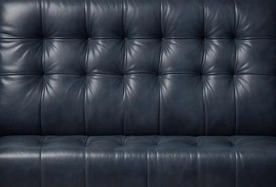 The primary subject of the image is a blue leather couch. The setting is a dark room, and the visual style is a close-up of the couch. The colors and mood of the image are predominantly dark and moody, with the blue leather couch being the main focal point.
