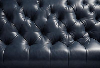 The primary subject of the image is a blue leather couch with a patterned design. The setting is a room with a blue background, and the visual style is a photo. The dominant colors in the image are blue and black, creating a modern and sophisticated atmosphere.