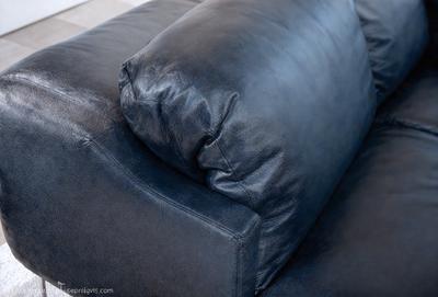 The primary subject of the image is a blue leather couch with a pillow on it. The setting is a room with a carpeted floor. The visual style is a photo, and the colors and mood are predominantly blue, creating a calm and relaxing atmosphere.