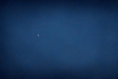 The primary subject of the image is a moon, which is visible in the sky. The setting is a dark blue sky, creating a contrasting backdrop for the moon. The visual style is a photo, capturing the moon in its natural environment. The colors and mood of the image are predominantly dark and moody, with the blue sky and the moon creating a sense of depth and tranquility.