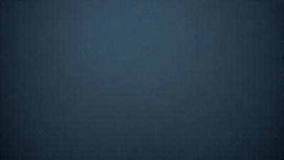 The primary subject of the image is a blue sky with a single dot in the middle of it. The sky appears to be cloudless, and the dot is located towards the center of the image. The setting is a vast, open space with no visible landmarks or objects. The visual style is a simple, minimalist representation of the sky, with no additional elements or colors. The colors and mood of the image are predominantly blue, creating a calm and serene atmosphere.