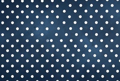 The primary subject of the image is a pattern of white dots on a blue background. The setting is a dark blue surface, which contrasts with the white dots. The visual style is a combination of a photo and a digital art, as the dots are arranged in a way that resembles a digital artwork. The colors and mood of the image are predominantly dark blue and white, creating a calm and serene atmosphere.