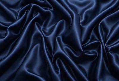The primary subject of the image is a blue fabric, which appears to be a piece of silk. The setting is a dark background, which contrasts with the blue fabric. The visual style is a close-up of the fabric, showcasing its texture and details. The colors and mood of the image are predominantly dark and moody, with the blue fabric being the main focal point.