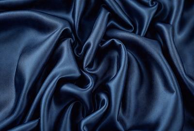 The primary subject of the image is a close-up of a blue fabric, possibly a piece of silk or velvet. The setting is a dark background, which emphasizes the richness of the blue fabric. The visual style is a close-up, which highlights the texture and details of the fabric. The colors and mood of the image are predominantly blue, creating a sense of calmness and sophistication.