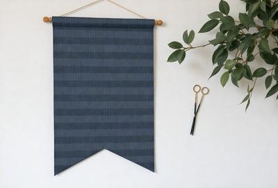 The primary subject of the image is a blue and white striped curtain hanging on a wall. The curtain is made of fabric and has a patterned design. The setting is a room with a wall, and the visual style is a photo. The colors and mood of the image are predominantly blue and white, creating a calm and serene atmosphere.