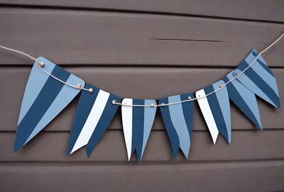 The primary subject of the image is a blue and white striped banner hanging from a wall. The banner is made of paper and features a design that resembles a kite. The setting is a wall, and the visual style is a combination of photo and digital art. The colors and mood of the image are predominantly blue and white, creating a calm and soothing atmosphere.