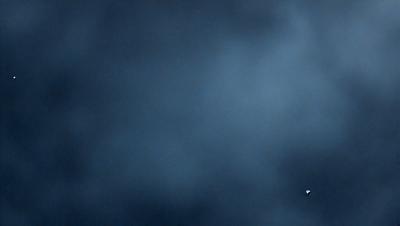 The primary subject of the image is a cloudy sky. The setting is a dark, cloudy night with a blue hue. The visual style is a photo, capturing the beauty of the night sky. The colors and mood are predominantly dark and moody, with the blue hue adding a touch of calmness to the scene.