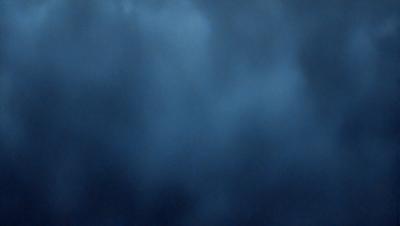 The primary subject of the image is a cloudy blue sky. The setting is a vast expanse of the sky, with no visible land or other objects. The visual style is a natural, outdoor scene. The colors and mood are predominantly blue, with a slightly gloomy atmosphere.