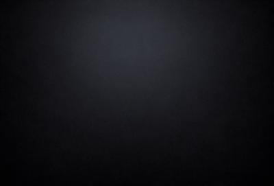 The image is a black and white photo of a dark background. The primary subject is a large, empty space with no visible objects or details. The setting is a black background, which creates a stark contrast with the subject. The visual style is a black and white photo, giving the image a classic and timeless appearance. The colors and mood are predominantly dark and moody, with the black background emphasizing the emptiness and simplicity of the scene.