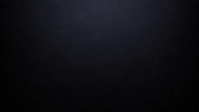 The primary subject of the image is a black background with a white dot in the center. The setting is a dark room, and the visual style is a simple, minimalist design. The colors are predominantly black and white, creating a stark and dramatic atmosphere.