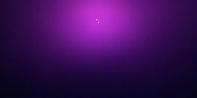 The primary subject of the image is a purple background with two small purple dots in the center. The setting is a dark, purple-colored environment, which creates a moody atmosphere. The visual style appears to be a digital art or illustration, as the purple dots are the main focus of the image. The colors and mood of the image are predominantly purple, giving it a unique and striking appearance.