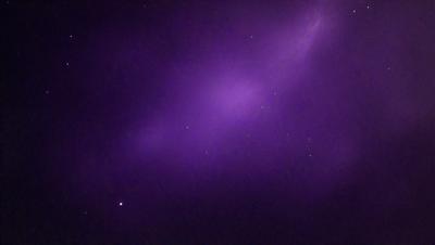 The primary subject of the image is a purple sky filled with stars. The setting is a dark, star-filled sky, and the visual style is a photo. The colors and mood of the image are predominantly purple, creating a serene and peaceful atmosphere.