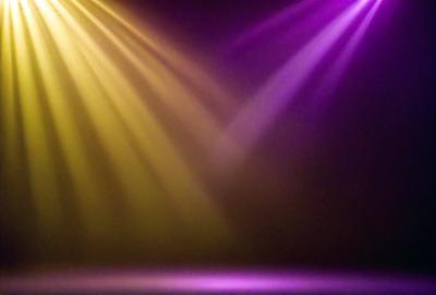 The primary subject of the image is a brightly lit stage with a purple and yellow light show. The setting is a darkened stage, and the visual style is a combination of photo and digital art. The colors and mood of the image are vibrant and energetic, creating a lively atmosphere.