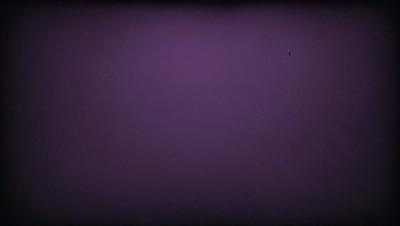 The image is a purple background with a black dot in the upper right corner. The background is a deep purple color, and the dot appears to be a small black circle. The overall atmosphere of the image is dark and moody, with the purple background creating a sense of mystery or intrigue.