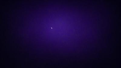 The primary subject of the image is a moon, which is the main object in the scene. The setting is a dark, purple sky, creating a moody atmosphere. The visual style is a photo, capturing the moon in its natural environment. The colors and mood of the image are dominated by the purple hue of the sky, which adds a sense of mystery and tranquility to the scene.