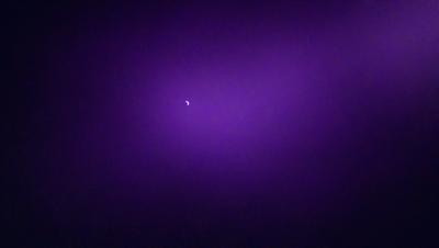 The primary subject of the image is a moon, which is the main object in the scene. The setting is a purple background, which creates a unique and visually striking atmosphere. The visual style of the image is a photo, capturing the moon in its natural environment. The colors and mood of the image are predominantly purple, giving it a serene and dreamy quality.