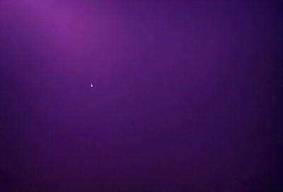 The primary subject of the image is a bright star in the purple sky. The setting is a dark, purple background, which contrasts with the bright star. The visual style is a photo, capturing the star and its surroundings. The colors and mood of the image are dominated by the purple hue, creating a serene and peaceful atmosphere.
