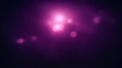 The primary subject of the image is a purple background with a cluster of bright lights. The setting appears to be a dark room, and the visual style is a combination of a photo and digital art. The dominant colors are purple and pink, creating a warm and inviting atmosphere.