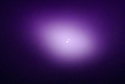 The primary subject of the image is a purple background with two small white dots in the center. The setting appears to be a dark, purple-hued environment. The visual style of the image is a digital art or illustration, as the purple background and the white dots are created with digital tools. The colors and mood of the image are predominantly purple, with a slightly mysterious and moody atmosphere.