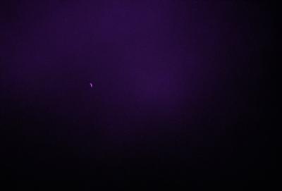 The image is a purple night sky with a single moon visible in the distance. The moon is located towards the left side of the image, and the sky appears to be dark and cloudy. The overall atmosphere of the image is serene and peaceful, with the moon being the main focus of the scene.