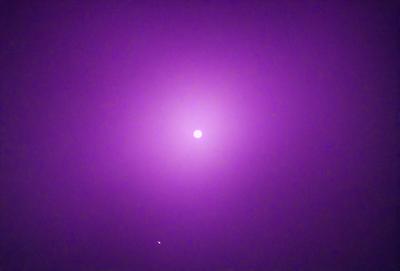 The primary subject of the image is a purple circle, which appears to be a celestial object, such as a planet or a moon. The setting is a dark, purple sky, which creates a dramatic and mysterious atmosphere. The visual style of the image is a combination of photo and digital art, giving it a unique and intriguing appearance. The colors and mood of the image are predominantly purple, which adds to the overall ambiance and moodiness of the scene.