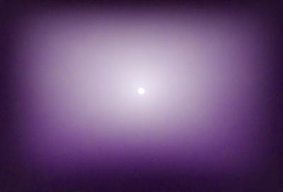 The primary subject of the image is a moon, which is the main object in the scene. The moon is located in the middle of the image, and it appears to be a bright, white, and round object. The setting is a dark, purple sky, which creates a dramatic and moody atmosphere. The visual style of the image is a photo, capturing the moon against the night sky. The colors and mood of the image are dominated by the purple hue of the sky, which gives the scene a sense