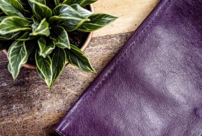 The primary subject of the image is a purple wallet, which is placed on a wooden table. The setting is a room with a wooden floor, and the visual style is a photo. The dominant colors in the image are purple and brown, creating a warm and cozy atmosphere.