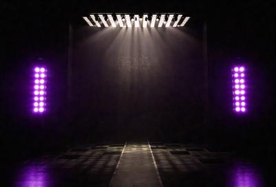 The primary subject of the image is a large, illuminated wall with a purple glow. The setting is a dark room, and the visual style appears to be a combination of a photo and digital art. The dominant colors are purple and black, creating a moody atmosphere.