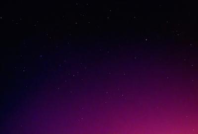 The primary subject of the image is the night sky, which is filled with stars. The setting is a dark, purple-colored sky, creating a dramatic and serene atmosphere. The visual style of the image is a photo, capturing the beauty of the night sky. The colors and mood of the image are predominantly purple, with the stars creating a sense of wonder and tranquility.