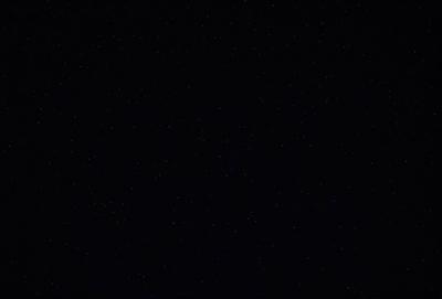 The primary subject of the image is the night sky, which is filled with stars. The setting is a dark, star-filled sky, and the visual style is a black and white photo. The colors and mood of the image are predominantly dark and moody, with the stars providing a sense of depth and beauty.