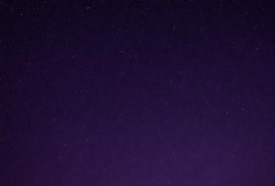 The primary subject of the image is the night sky, which is filled with stars. The setting is a dark, star-filled sky, and the visual style is a photo. The colors and mood of the image are predominantly dark and serene, with the stars providing a sense of depth and beauty.