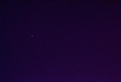 The primary subject of the image is the night sky, which is filled with stars. The setting is a dark, purple background, creating a dramatic and serene atmosphere. The visual style is a natural, outdoor scene, with no indication of being a photo, digital art, illustration, drawing, pattern, texture, or clipart. The colors and mood are predominantly purple, with the stars providing a sense of depth and beauty.