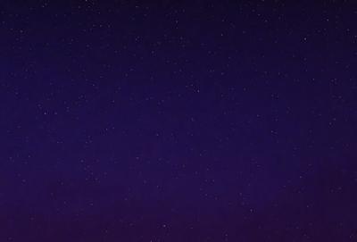 The primary subject of the image is the night sky, which is filled with stars. The setting is a dark, star-filled sky, and the visual style is a photo. The colors and mood of the image are predominantly dark and serene, with the stars providing a sense of depth and beauty.