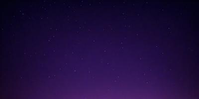The primary subject of the image is the night sky, which is filled with stars. The setting is a dark, purple-colored background, creating a dramatic and serene atmosphere. The visual style is a natural, outdoor scene, with no indication of being a photo, digital art, illustration, drawing, pattern, texture, or clipart. The colors and mood of the image are predominantly purple, with the stars providing a sense of depth and beauty.