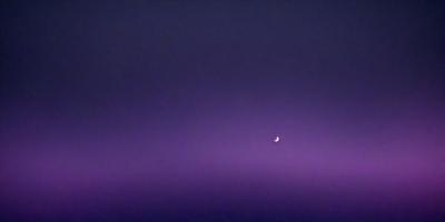 The primary subject of the image is a moon, which is the main object in the scene. The setting is a purple sky, creating a serene and peaceful atmosphere. The visual style is a photo, capturing the beauty of the moon in the night sky. The colors and mood of the image are dominated by the purple hue, which adds a sense of calmness and tranquility to the scene.