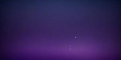 The primary subject of the image is the night sky, which is filled with stars. The setting is a dark, purple-colored background, creating a dramatic and serene atmosphere. The visual style is a combination of a photo and digital art, as the image captures the beauty of the night sky while also showcasing the artistic elements of the purple background. The colors and mood of the image are predominantly purple, which adds to the overall ambiance of the scene.