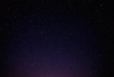 The primary subject of the image is the night sky, which is filled with stars. The setting is a dark, star-filled sky, and the visual style is a photo. The colors and mood of the image are predominantly dark and serene, with the stars providing a sense of depth and beauty.