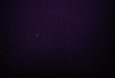 The primary subject of the image is a crescent moon, which is the main object in the scene. The moon is set against a dark, purple sky, creating a dramatic and moody atmosphere. The visual style of the image is a photo, capturing the moon and its surroundings in a realistic manner. The colors and mood of the image are predominantly dark and mysterious, with the purple sky adding a touch of elegance to the scene.