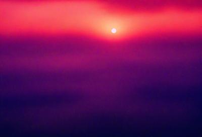 The primary subject of the image is a sunset, with the sun peeking through the clouds. The setting is a purple sky, which adds a unique and artistic touch to the scene. The visual style is a combination of a photo and digital art, creating a captivating and visually appealing image. The colors and mood of the image are predominantly purple, which gives it a serene and dreamy atmosphere.