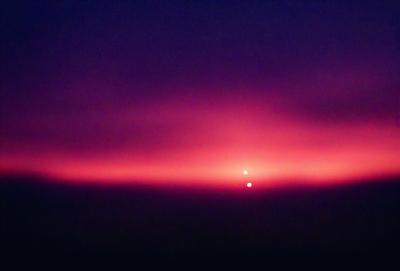 The primary subject of the image is a sunset, with the sun setting in the distance. The sky is a mix of purple and pink hues, creating a beautiful and serene atmosphere. The setting is a cloudy sky, which adds to the overall visual style of the image. The colors and mood of the scene evoke a sense of tranquility and awe, as the sun sets and the day comes to an end.
