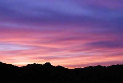 The primary subject of the image is a beautiful sunset with a purple sky. The setting is a mountain range, with the sun setting behind the mountains. The visual style is a photo, capturing the stunning colors and atmosphere of the sunset. The dominant colors are purple and orange, creating a serene and picturesque scene.