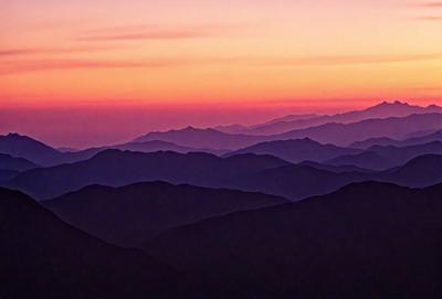 The image features a beautiful mountain range with a purple sky in the background. The mountains are covered in a dark, rich color, and the sky above them is a vibrant shade of purple. The scene is a stunning representation of nature, with the mountains stretching across the entire image and the sky providing a dramatic backdrop.