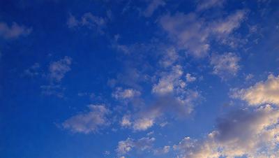 The primary subject of the image is a cloudy blue sky. The setting is a vast expanse of the sky, with no visible land or other objects. The visual style is a natural, outdoor scene. The colors and mood are predominantly blue and serene, with the clouds adding a sense of depth and movement to the sky.