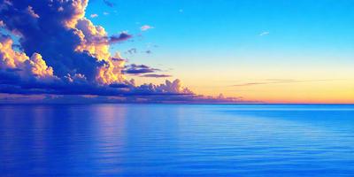 The primary subject of the image is the vast ocean, with a beautiful blue color. The setting is a cloudy sky, which adds a dramatic backdrop to the scene. The visual style is a photo, capturing the natural beauty of the ocean and the sky. The colors and mood of the image are serene and calming, with the blue ocean and the cloudy sky creating a peaceful atmosphere.