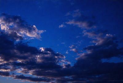 The primary subject of the image is a cloudy blue sky with a few clouds scattered throughout. The setting is a vast, open sky, and the visual style is a natural, outdoor atmosphere. The colors and mood of the image are predominantly blue and calm, with the clouds adding a sense of depth and movement to the sky.