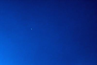 The primary subject of the image is the moon, which is visible in the sky. The setting is a clear blue sky, with no clouds or other obstructions. The visual style is a photo, capturing the moon and the sky in a natural and unaltered manner. The colors and mood of the image are predominantly blue, creating a serene and peaceful atmosphere.