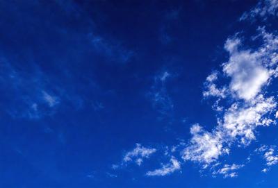 The primary subject of the image is the sky, which is a deep blue color. The setting is a cloudy day, with the clouds scattered throughout the sky. The visual style of the image is a photo, capturing the beauty of the cloudy sky. The colors and mood of the image are serene and peaceful, as the blue sky contrasts with the white clouds.